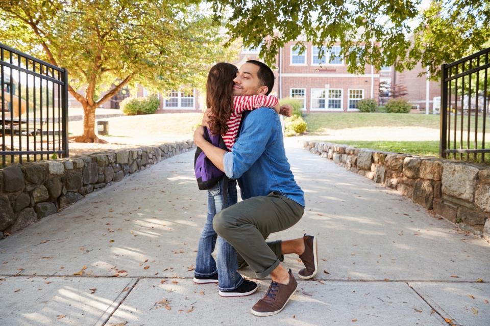 Dad hugging daughter on sidewalk. 