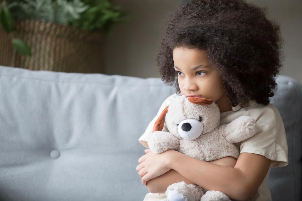 Little girl looking concerned hugging teddy bear.