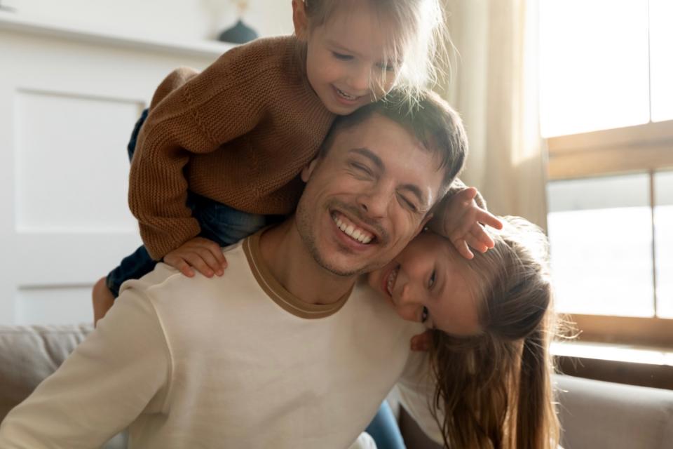 Smiling father is hugged from behind by his two young daughters