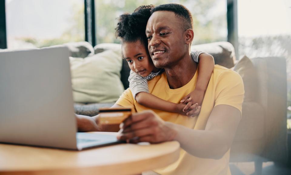 Man holds credit card and shops online while his daughter hugs him from behind