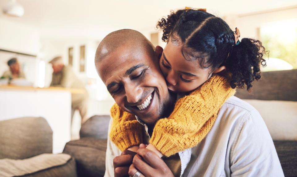 A father is hugged and kissed from behind by his young daughter.