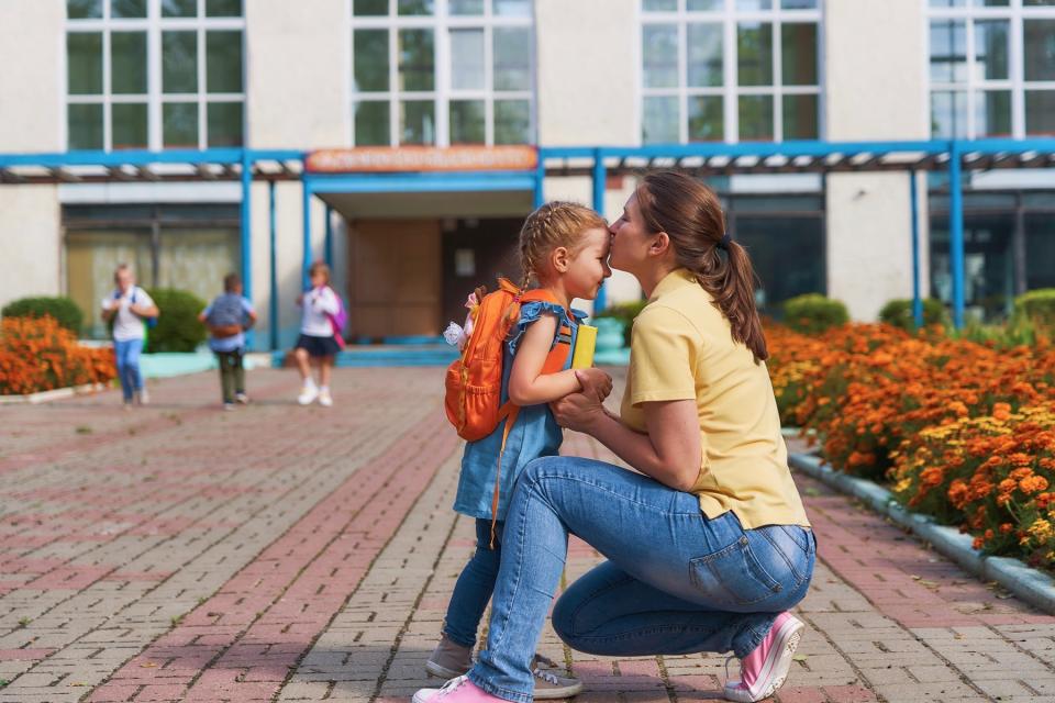 Mom kissing daughter outside of school.