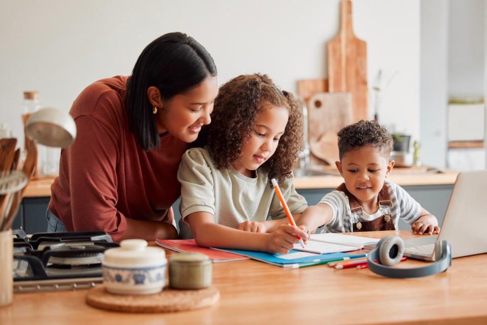 A mother and her young son and daughter do schoolwork together at a table.