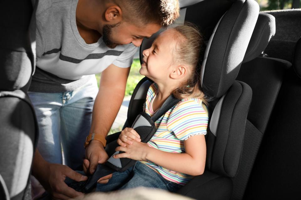 Man buckling his daughter into carseat.