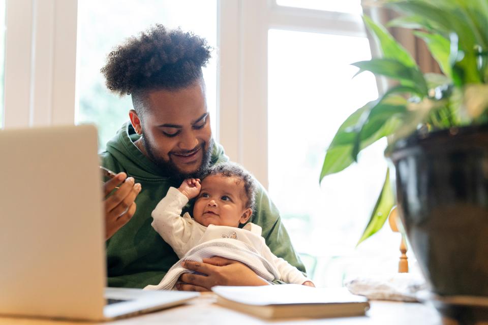 A father holds his infant while working on a computer.