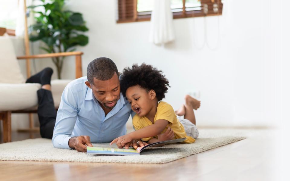 Dad and young child reading a book on floor. 