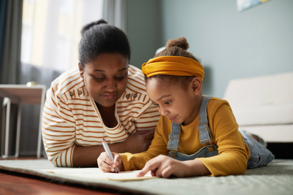 Une mère et sa fille sont allongées par terre pendant que la fille dessine.