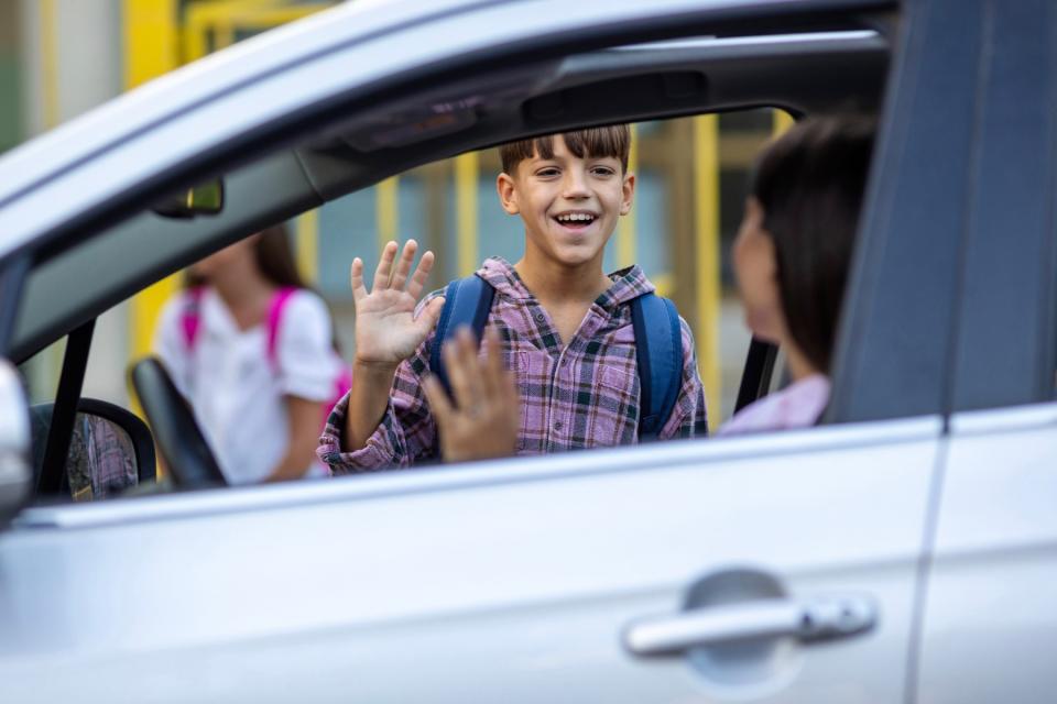 Mom waving to son from car at school drop-off.