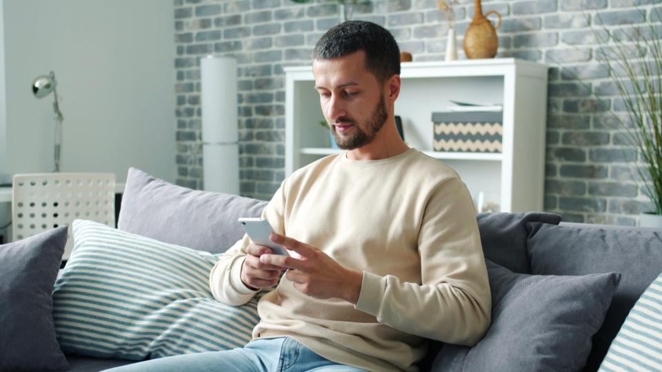 Dad calmly reading text message on couch. 