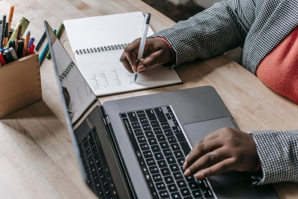Woman filling out planner while looking at laptop.