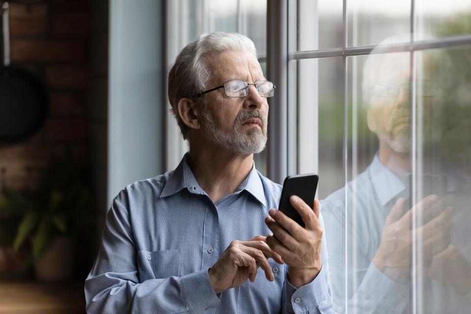 Worried parent looking out a window while holding a phone