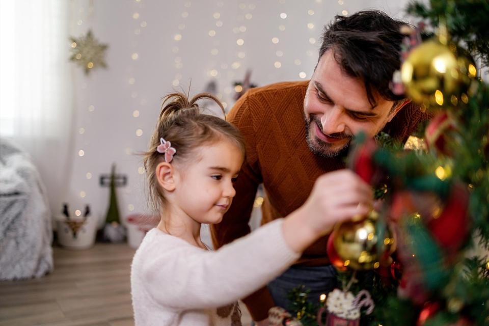 Father and young daughter hanging ornaments on a Christmas tree at home