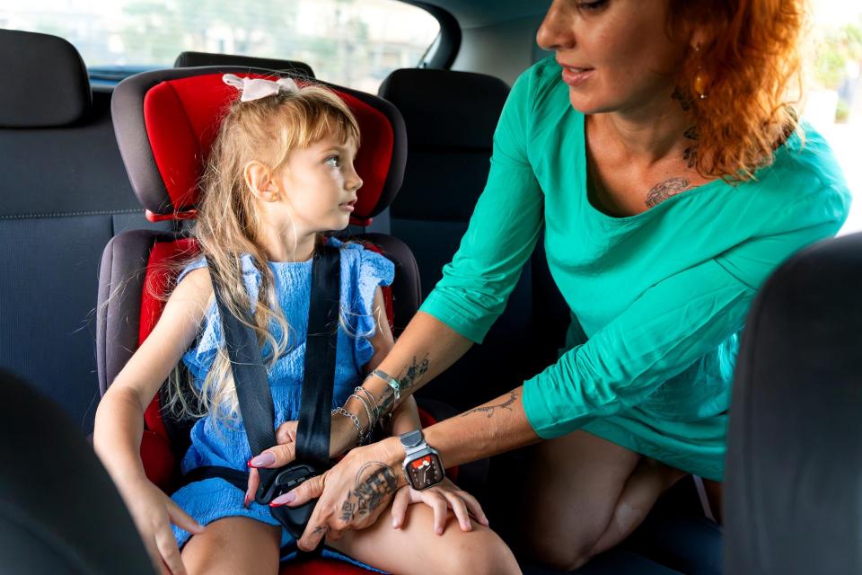 Mother buckling her daughter into a car seat before a family road trip